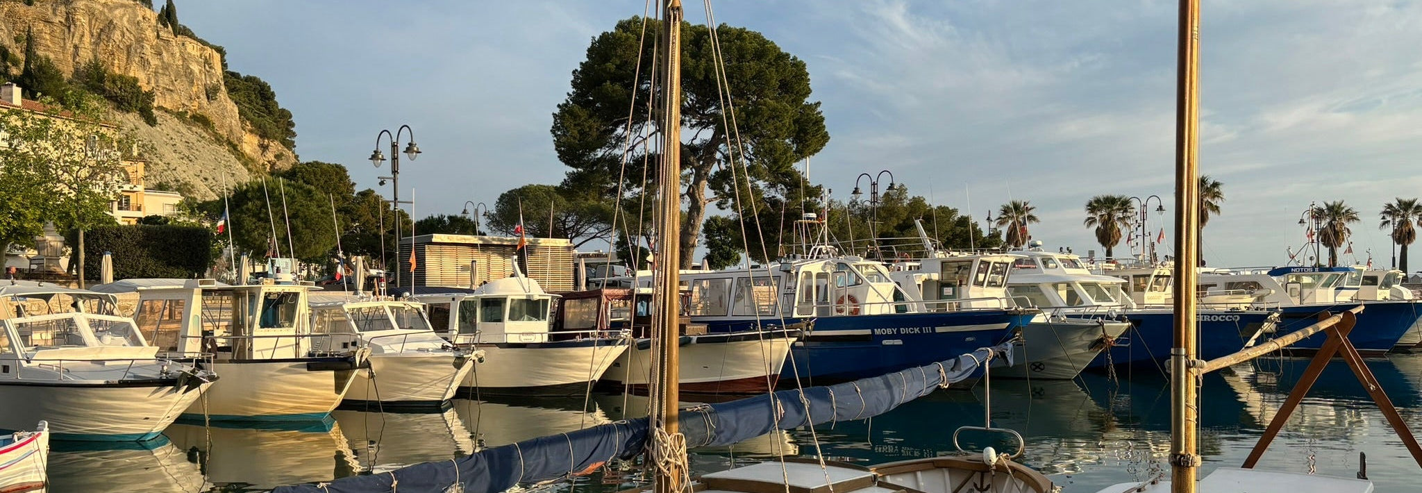 Marina with boats docked along a waterfront, with a mountainous landscape in the background.