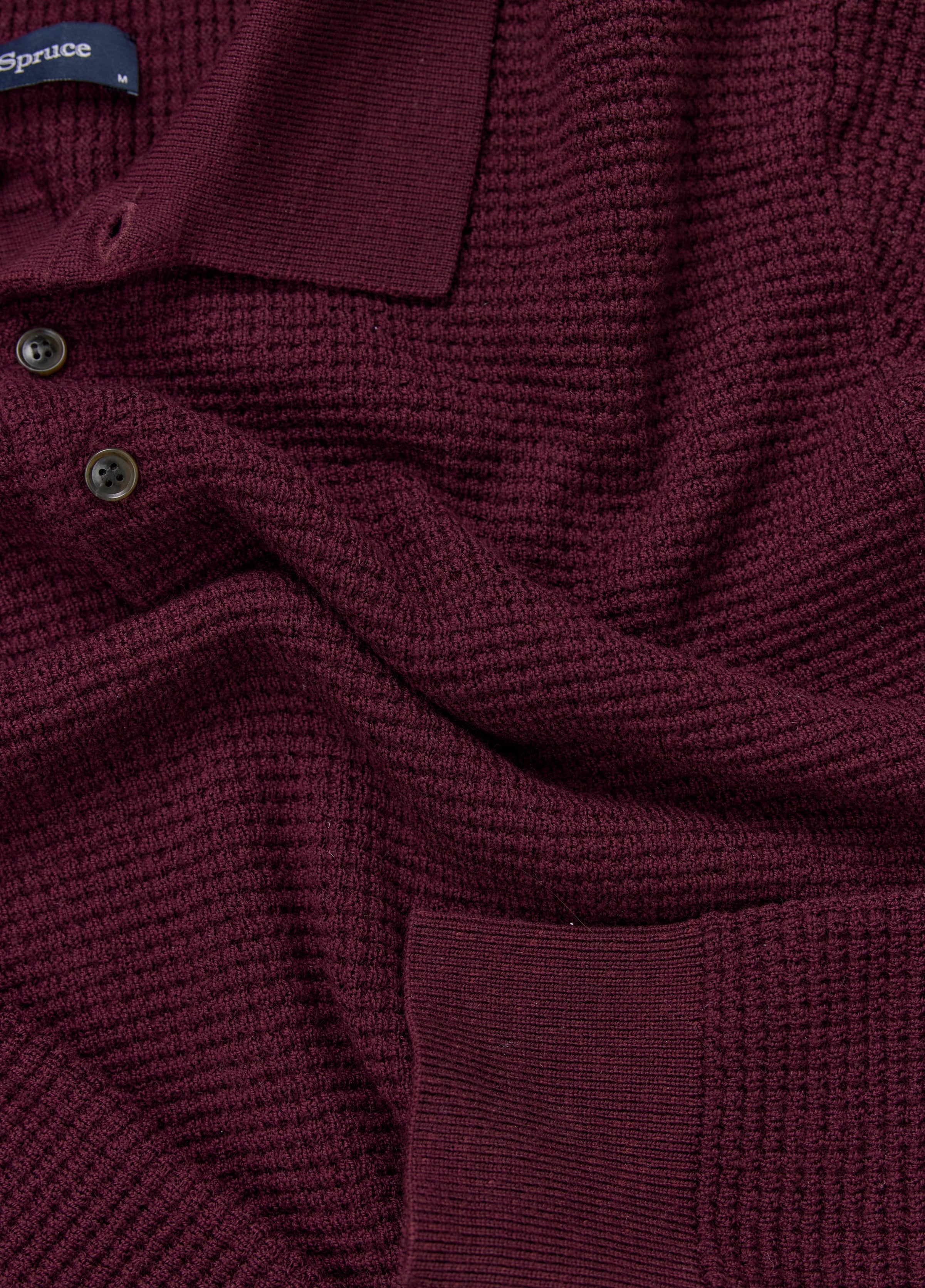 Close-up of a textured burgundy sweater with buttons and a brand label.